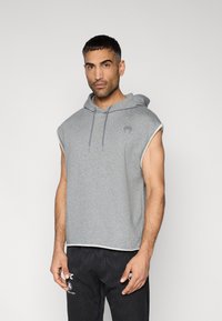 Γκρι αμάνικο φούτερ με κουκούλα από βαμβακερό μείγμα, με μπροστινή τσέπη, κουκούλα με κορδόνι και διακριτικό λογότυπο στο στήθος. Μαλακή υφή.