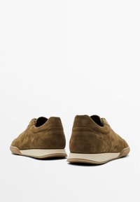 Sneaker in suede marrone con profilo basso, punta tonda e suola in gomma leggera. Texture liscia con cuciture minime e senza hardware visibile.