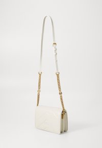 Λευκή δερμάτινη τσάντα ώμου με σχέδιο ζιγκ-ζαγκ, χρυσές αλυσίδες και ρυθμιζόμενη ζώνη. Συμπαγής ορθογώνια μορφή.