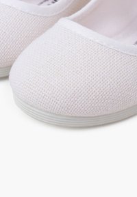 Zapatillas slip-on de lona blanca con un upper texturizado, puntera redonda y suela de goma blanca. Detalles de costura alrededor del cuello.