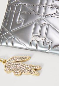 Portafoglio silver con motivo geometrico e finitura metallica, dotato di un portachiavi decorato con strass dorati a forma di coccodrillo.