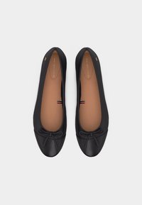 Ballerine nere in pelle con piccoli fiocchi sulle punte, suole interne beige e dettagli sottili con il logo.