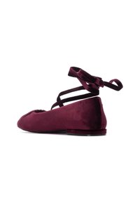 Zapato tipo ballerina en terciopelo burdeos con puntera redondeada y tacón plano. Presenta cintas de ante en el tobillo atadas en la parte posterior.
