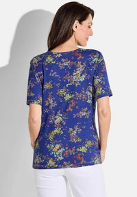 Blusenshirt mit kurzen Ärmeln in Blau, ausgestattet mit einem lebhaften Print aus gelben, pinken und weißen Blumen, aus einem weichen Baumwollmischgewebe gefertigt.