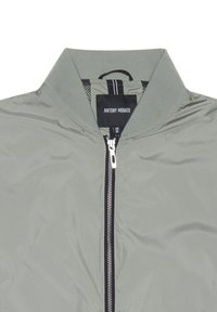 Giacca bomber verde oliva chiaro con colletto rialzato, zip frontale completa e traccia della zip nera. Presenta un motivo a scacchi sul tessuto.