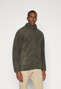 Grüne Fleecejacke mit hohem Kragen, Reißverschluss vorne, Seitentaschen und Logo-Patch auf der Brust. Weicher Stoff und lässige Passform.