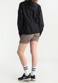 Giacca leggera nera con cappuccio, pantaloni corti beige, scarpe da ginnastica nere e calze bianche con strisce nere. Focalizzato sulla funzionalità e sul comfort.