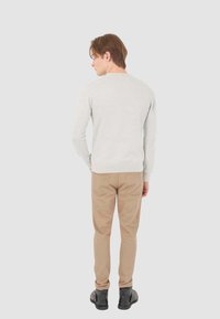 Maglione grigio chiaro a maglia con orlo a costine, abbinato a pantaloni beige slim-fit e scarpe nere, visto da dietro.