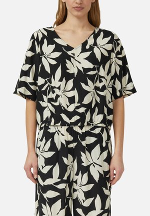 Vrouw draagt een zwart-wit bloemenpatroon top met korte mouwen en bijpassende broek met een losse pasvorm.