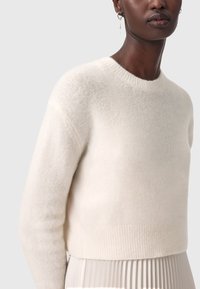 Pullover in lana color crema con scollatura tonda, spalle scese e orlo a coste. Tessuto morbido, design leggermente corto.