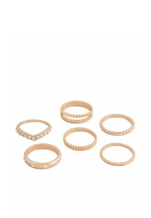Sechs goldfarbene Ringe, einige mit eingearbeiteten klaren Steinen, auf weißem Hintergrund angeordnet, mit unterschiedlichen Texturen und Mustern.
