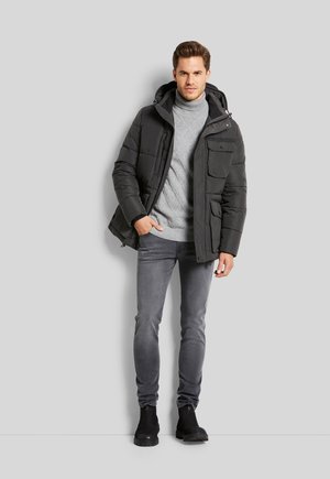 Schwarze Daunenjacke mit Kapuze, vordere Taschen, grauer Strickpullover, graue Jeans und schwarze Stiefel. Glatte Textur, lässiges Design.