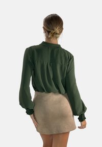 Groene textuurblouse met lange mouwen en gather manchetten, gecombineerd met een lichtbruine suède minirok.