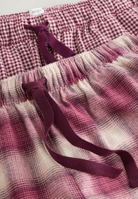 Rutiga shorts i nyanser av rosa och kräm, med resårmidja och dragsko. Har ett rutmönster och en mjuk textur.