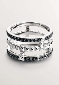 Anillos apilados hechos de metal en tono plateado presentan acentos de piedra negra y formas piramidales, exhibiendo un diseño geométrico moderno con un acabado brillante.