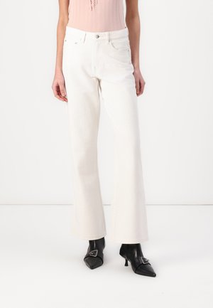 White flared jeans with a high waist, made of denim, featuring a smooth texture and minimal stitching. Paired with black heeled boots.