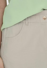 Top verde claro combinado con pantalones beis claros que presentan un bolsillo frontal y un cierre con botón metálico. Tela suave, diseño casual.