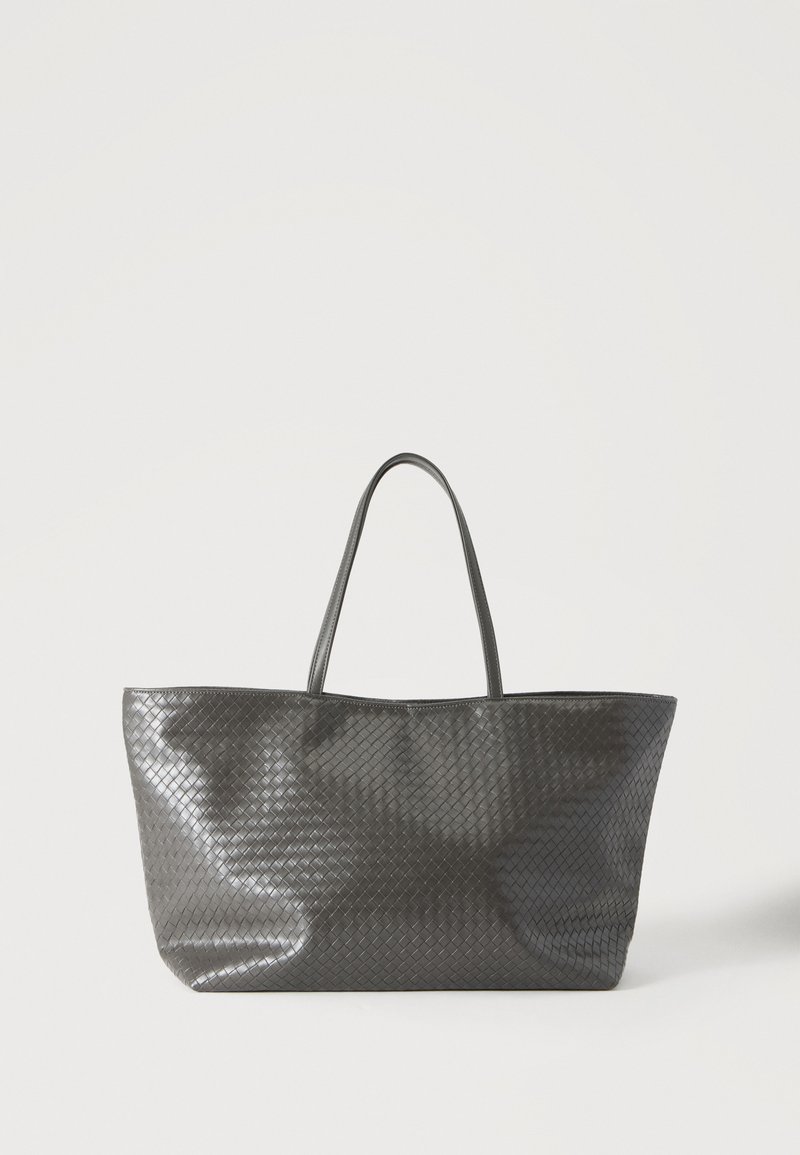 Sac cabas en cuir tissé noir avec deux poignées, debout sur un fond clair.