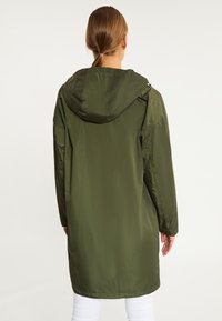 Jachetă parka impermeabilă de culoare verde măslinie, cu glugă, mâneci lungi și croială dreaptă. Prezintă o textură netedă și detalii de cusătură subtile.