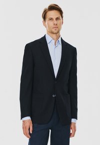 Czarna marynarka z klapami, dwoma przednimi kieszeniami, zapięciem na jeden guzik i teksturowanym materiałem, zestawiona z jasnoniebieską koszulą.