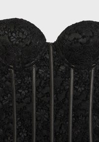 Corset en dentelle noire avec motifs floraux et armature structurée, présentant des bonnets moulés et des bordures satinées verticales à l'avant.
