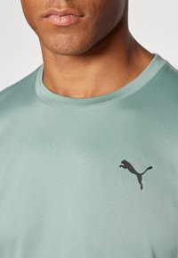 Camiseta deportiva de manga corta verde menta con cuello redondo y logo negro de Puma en el pecho; textura de tela suave y ligera.