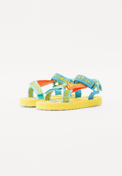 Felgekleurde sandalen met een gele zool, blauwe en oranje banden met de tekst "IMAGINATION," gemaakt van rubber en stof.