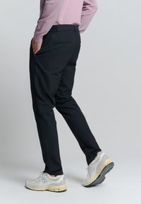 Zwarte sportbroeken met een elastische tailleband, zijzakken en een tapered ontwerp, gecombineerd met lichtgrijze en gele sneakers.