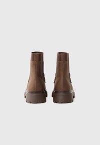 Bruine leren enkelboots met een gestructureerde afwerking, elastische zijkanten en dikke, robuuste zolen. De achterkant heeft aantrek-luiken voor gemakkelijk aan- en uittrekken.