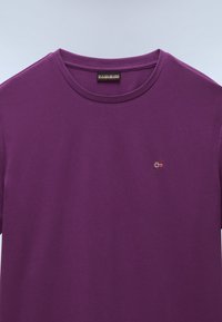 Purple cotton t-shirt with short sleeves and a round neckline. Features a small embroidered patch with a flag design on the chest.