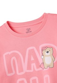 Camiseta de color rosa claro con un gran oso de dibujos animados que lleva un gorro de dormir y la palabra "NAP" en letras grandes. Material de algodón suave.