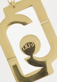 Χρυσών μεταλλικό αξεσουάρ με γεωμετρικό σχέδιο και κυκλική λεπτομέρεια, με κομμένο το «LIU·JO» σε αντίθετη απόχρωση.