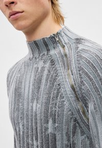 Πλεκτό πουλόβερ σε γκρι με ψηλό γιακά και φερμουάρ. Κατακόρυφες ρίγες και υφασμένα μοτίβα σε όλο το ένδυμα, με αντίθετη λεπτομέρεια σε ανοιχτό μπλε.