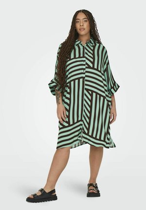 Kurzärmliges, oversized Hemdkleid in mintgrünen und braunen vertikalen Streifen. Verfügt über eine durchgehende Knopfleiste und zwei Seitentaschen. Trägt schwarze Sandalen.