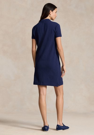 Granatowa sukienka polo z bawełny, z kołnierzykiem, krótkimi rękawami, bocznymi rozcięciami i luźnym krojem, noszona z pasującymi wsuwanymi butami.