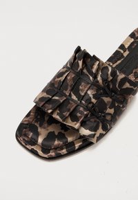 Mules à imprimé léopard avec dessus en tissu, présentant des plis et des accents de nœud noir. Bout ouvert avec une semelle plate.