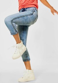 Svetle modré džíny s ohrnutým lemem a vybledlým omakem, s kontrastním bočním švem a zipem. Kombinované s bílými vysokými teniskami.