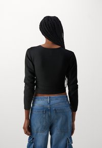 Must mustriba pikka varrukaga crop top mustas värvitoonis, ümarate kaelustega, koos siniste cargo teksadega, millel on tagakotid ja küljetaskud.
