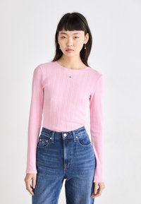 Langærmet, ribbet pink top med en bølget halsudskæring og lille logo detalje. Sammen med højtaljede blå jeans.