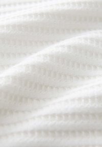 White fabric with a textured pattern featuring diagonal lines and small gaps, creating a soft and lightweight appearance.
