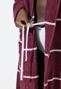 Robe bordeaux con texture e strisce bianche, tenuto insieme in modo rilassato da un nastro bianco, che mostra in parte un indumento intimo bianco sottostante.