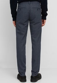 Pantaloni a quadri grigi realizzati in tessuto testurizzato, caratterizzati da una vestibilità su misura, due tasche posteriori con bottoni e un design frontale piatto.