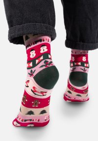 Dzianinowe skarpetki z różowym tłem, ozdobione wzorami bałwanków, choinek, piernikowych ludzików oraz Świętego Mikołaja, z zielonymi akcentami.