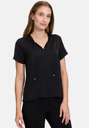Blusa nera a maniche corte con scollo a V e cordino. Tessuto morbido con una leggera lucentezza, presenta una vestibilità rilassata e dettagli minimi.