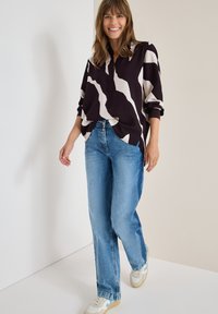 Camicia leggera di un viola scuro con un motivo astratto crema, maniche arrotolate; abbinata a jeans azzurri a vita alta e sneakers bianche.
