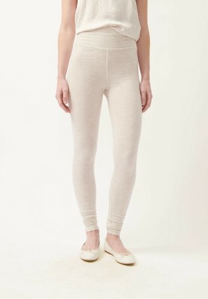 Light beige leggings made of a soft, textured fabric, featuring a high waistband that fits snugly, paired with simple flat shoes.