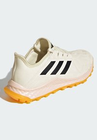 Chaussure de course Adidas avec une tige crème, des rayures noires et une semelle intermédiaire rose texturée. Présente une semelle extérieure jaune avec des détails de traction.