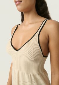Abito beige a coste con bordi neri, caratterizzato da un scollo a V e un corpetto texturizzato, che si restringe verso una gonna ampia con dettagli orizzontali.
