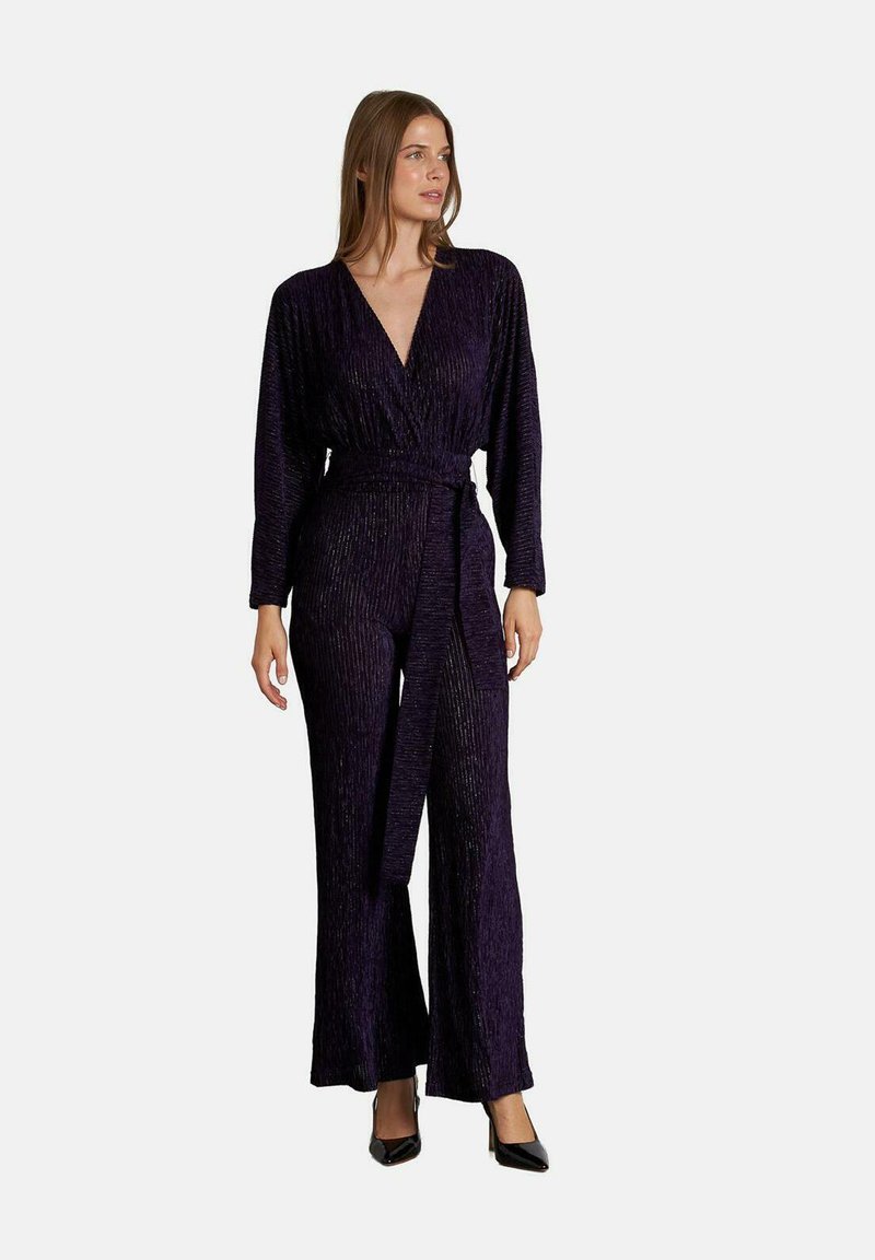 Mono morado con mangas largas, escote en V profundo, tejido texturizado, cintura ceñida y pantalones de pierna ancha, complementado con un cinturón de tela.