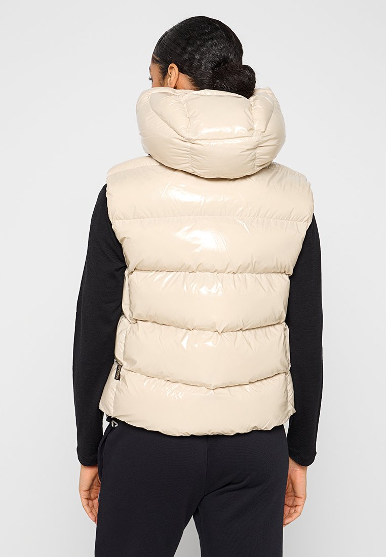 Beige, gefütterte Weste mit glänzender Optik, hohem Kragen und horizontalen Nähten. Getragen über einem schwarzen Langarmoberteil. Einfaches Design, lockere Passform.